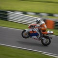 A panning shot of an orange/white racing bike on one wheel