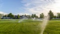 Pano frame Park with sprinklers watering the vibrant green grasses on a sunny day