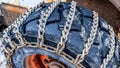 Pano Huge black wheel of a bulldozer wrapped with rusty chains against snow