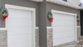 Pano White garage doors of home with festive wreaths mounted on the gray wall