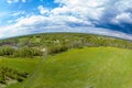 Panorama aerial view of green meadow and field near the path in the form of a small planet around which are gray and white clouds Royalty Free Stock Photo