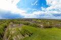 Panorama aerial view of green meadow and field near the path in the form of a small planet around which are gray and white clouds Royalty Free Stock Photo