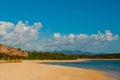 Panorama of beautiful tropical landscape: yellow sand, blue Caribbean sea, coconut palm trees, umbrellas are for tourists. Mountai