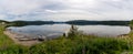 Panorama of a calm lake with reflections of mountains and sky and canoes and boat in the foreground