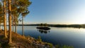 Panorama of a calm lake with small island and golden sunset evening light on the trees and forest on the lakeshore in the Royalty Free Stock Photo