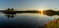 Panorama of a calm lake with small island and golden sunset evening light on the trees and forest on the lakeshore in the Royalty Free Stock Photo