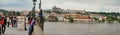 Panorama of the Charles Bridge and Vltava River in Prague, with people on the bridge and historic buildings on the riverbank