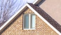 Panorama Close up of a home exterior with sunlit pitched roof over window and brick wall