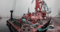 Panorama: Close-up view of cargo port in fog. Tug, floating crane, dry cargo s