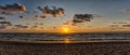 Panorama of a colorful beach sunset with the sun dropping into the ocean under an expressive sky Royalty Free Stock Photo