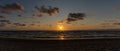 Panorama of a colorful beach sunset with the sun dropping into the ocean under an expressive sky Royalty Free Stock Photo