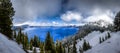 Panorama of Crater Lake with deep blue water, grand cloudy sky and snow covered trees in the foreground Royalty Free Stock Photo