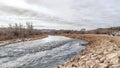 Panorama crop Glistening river with grassy and rocky banks along houses and hill landscape Royalty Free Stock Photo