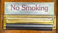 Panorama crop No Smoking sign above mail drop slot with black tape against brown wood door