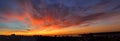 Panorama of dawn fire in the sky over a small seaside city. Golden red clouds just before the sunrise. Scenic landscape at sunrise