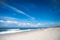 Panorama of a deserted sandy beach on which the sea foamy waves roll. An endless blue sky with white clouds on it.