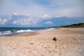 Panorama of a deserted sandy beach on which the sea foamy waves roll. An endless blue sky with white clouds on it.