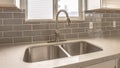 Panorama Double bowl stainless steel sink against tiled wall with window and cabinets