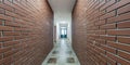 panorama in empty long corridor with red brick walls and doors in interior of modern office