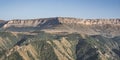 Panorama in the evening in the mountains of the Caucasus on a steep rocky slope of a table mountain and wooded hills with trees Royalty Free Stock Photo