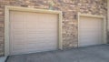 Panorama frame White garage doors of a home against exterior wall covered with stone bricks