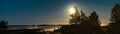 Panorama of full golden Moon close to pine trees, late summer night with clear skies and tiny white fog over water and coast line Royalty Free Stock Photo