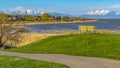 Panorama Grassy field with pathway and bench overlooking lake and mountain against sky