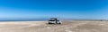 Panorama of a gray camper van parked on an endless white sand beach in the middle of nowhere with ocean behind