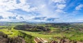 Panorama on hilly area with forests, fields, houses and highways in sunlight against a cloudy sky Royalty Free Stock Photo