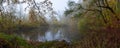 Panorama of lake surrounded by forest trees in misty autumn day Royalty Free Stock Photo