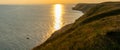 Panorama landscape of a beautiful ocean coast with grassy hills and warm sunshine and golden evening sunseet sky