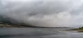 Panorama landscape view of a fjord with mystical fog and cloud cover coming down from the mountains over the ocean