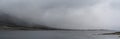 Panorama landscape view of a fjord with mystical fog and cloud cover coming down from the mountains over the ocean