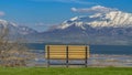 Panorama Lush field with an empty bench facing a snow peaked mountain and calm lake