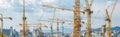 Panorama with many tower cranes in clear blue sky with clouds