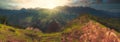 Panorama mountain range and valley at sunset in the background the sun just visible over the peaks and the last light highlighting