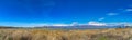 Panorama of a mountain with snowy peak towering over a lake with grassy shore