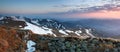 Panorama with mountains. The top of the hills covered with snow. The meadow with the rocks and yellow grass. Sunrise.