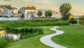 Panorama Pond and pathway on a scenic park in front of sunlit houses under cloudy sky