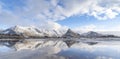 Panorama reflection of snowy mountains, blue sky and clouds on the calm clear water on a beach. Royalty Free Stock Photo