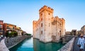 Panorama of Scaligero Castle or Castle of Sirmione surrounded by water canals of the Garda lake. People walking by the streets of