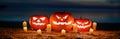 Panorama of Scary pumpkin lanterns with an evil Halloween grin. with lit candles in the sand on the seashore