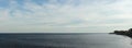 panorama of the sea strecthing out into the bay with a calm sea and cloud filled blue sky