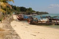 Panorama seascape dayshot of a white yellow sand beach with long boats, palm trees, mountains, turquoise ocean water and a blue