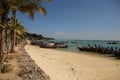 Panorama seascape dayshot of a white yellow sand beach with long boats, palm trees, mountains, turquoise ocean water and a blue