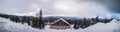 Panorama shot -Winter view overlooking a lodge in the mountains surrounded by evergreens and snow on a cloudy day, in Ranca resort Royalty Free Stock Photo