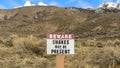 Panorama Sign that reads Beware Snakes May Be Present on a grassy mountain
