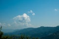 A panorama of successive mountain slopes, lost in a haze, against a background of blue sky and white cumulus clouds.