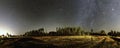 Panorama of very clear deep starry skies with Milky Way above harvested field and wild Scandinavian pine forest, autumn time