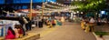 Panorama view blurry people at waterfront boardwalk string lights, beach chairs, patio restaurant dining tables blue hour with Royalty Free Stock Photo